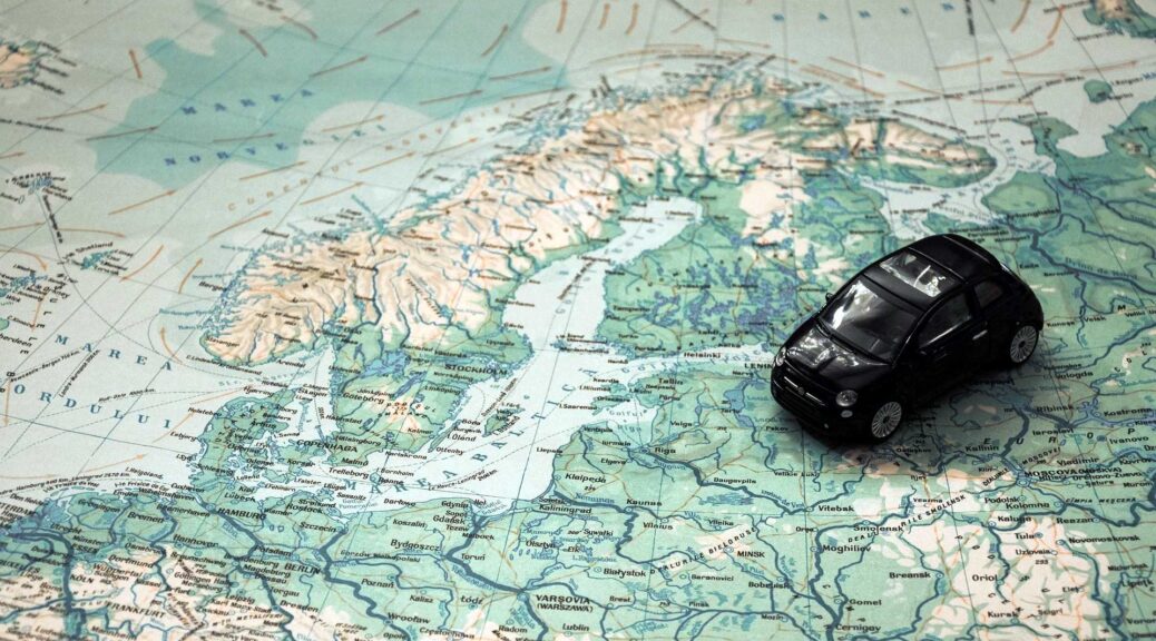 Czarny model samochodu umieszczony na szczegółowej mapie Europy Północnej, symbolizujący podróż samochodem